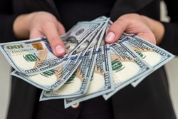 business lady in a black classic suit holds a bunch of new dollars in her beautiful hands. Business lady and business concept