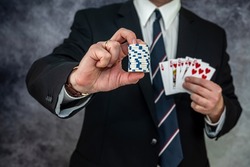 Stylish man in black suit holding play cards and poker chips in casino. Gambling  playing concept