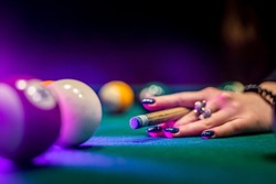 you can see beautiful female hands in black clothes deftly holding a cue and trying to drive a billiard layer into the hole. Billiards sport game concept
