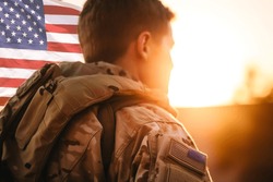 Rear view of a U.S. soldier looking at the sunset and a U.S. national flag.