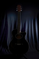 low key image of the silhouette of an acoustic guitar on a stage with a lightly illuminated black backdrop curtain in the background