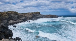 a sea with strong swell beating against the walls of a rocky cliff, blue rough sea with big waves with foam crashing against the rocks, Menorca, Balearic Islands, Spain