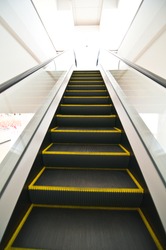 Escalator with yellow strips and glassy stair railing leading downstairs. Portrait orientation