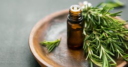 Rosemary essential oil bottle with rosemary herb bunch on wooden plate, aromatherapy herbal oil