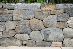 Dry stone wall and drain pipe, detail. Closeup of retaining wall between garden and sidewalk. Rounded edge fieldstone and flagstone variation, large and small, gray and brown, dry-stacked, natural.