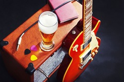 Tube combo amplifier for electric guitar with guitar, glass of beer and notepad on the black background. 