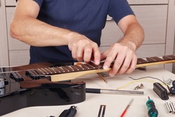 Guitar master burnishes the edge of frets on neck of the guitar.