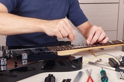 Guitar repairer checks leveling of frets on neck of the modern guitar.