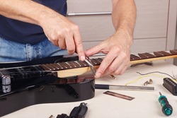 Guitar technician burnishes the edge of frets on neck of the electric guitar.