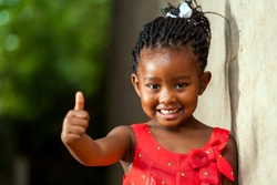 Portrait of happy little african girl doing thumbs up sign outdoors. 