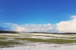 spring landscape in Europe. melting snow, green grass and blue skies with clouds.
