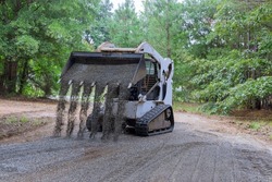 The mini loader Bobcat tractor moves and unloads gravel on the old road reconstruction site