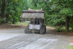 During the reconstruction of an old road, a transports Bobcat tractor is moving and unloading gravel