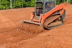 Using a small tractor to level the land near a new house using earth moving equipment in construction site
