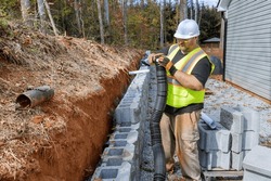 Construction worker of laying drainage pipe for rainwater in during mounting retaining wall.