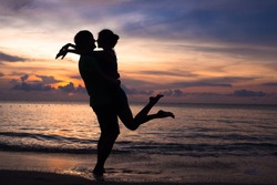 sunset silhouette of young couple in love hugging at beach