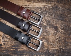 Men's leather trouser belts in the background of aged wood. Men's fashion accessories closet. Genuine leather, handmade
