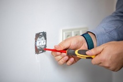 Man doing electrics. Close up of man installing electrical outlet in wall in room of house. Male electrician uses screwdriver to tighten bolts while attaching metal part of socket to wall.
