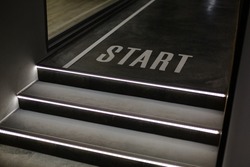 Staircase in building. Close up of dark staircase with LED backlight and with inscription Start. Selective focus detail in new building such as concrete steps with white LED illumination