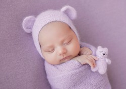 Newborn baby girl on a gray background in a hat with ears. A sweet newborn baby is sleeping. The first photo session of the baby. 