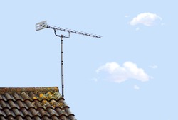 A tv aerial on a tiled roof top isolated against a blue sky with clouds 