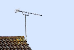A tv aerial on a tiled roof top isolated against a clear blue sky