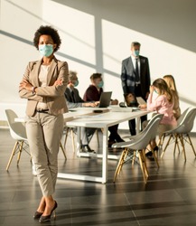 African American woman standing in the office in front of her team and wear facial mask as protection from corona virus