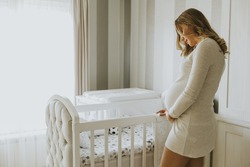 Portrait of pregnant woman setting up baby crib in the room