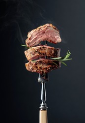 Grilled ribeye beef steak with rosemary on a black background.  Beef steak on a fork.