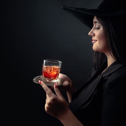 Attractive girl with alcoholic drink in frozen glass. Beautiful brunette in black hat holding glass with cold cocktail.