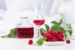 Raspberry liquor and fresh berries with leaves on a white wooden table.