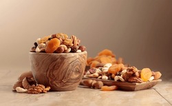 Dried fruits and nuts on a beige ceramic table. The mix of nuts, apricots, and raisins in a wooden bowl. Copy space.