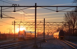Two trains leaving a railway station during a winter sunrise.