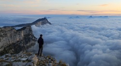 A hiker looking over a sea of clouds in the mountains at dawn. 