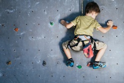 little boy climbing a rock wall indoor. Concept of sport life.