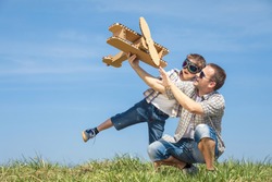 Father and son playing with cardboard toy airplane in the park at the day time. Concept of friendly family. People having fun outdoors. Picture made on the background of blue sky.