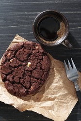 Large chocolate cookie and cup of coffee on black wooden background, top view