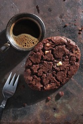 Large chocolate fudge cookie and cup of coffee on grunge metal background, top view