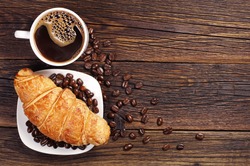 Coffee cup with croissant for breakfast on a dark wooden table, top view