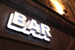 View of luminous bar signboard on wall of building at night