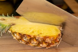 Close-up view of a cleaver in half a pineapple fruit on a cutting board in a domestic kitchen