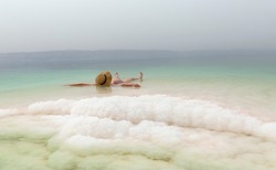 young woman with hat floating in the waters of the Dead Sea 