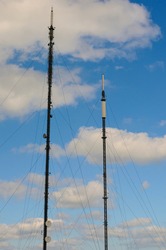 Two UK television and radio masts against a blue sky with clouds.