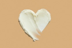 Shea butter cream textured heart shape smear on beige brown colour background, hair and skin care love swatch