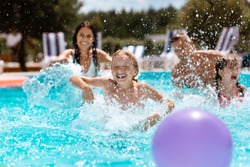 Ball in pool. Cheerful happy parents and children laughing while playing ball in swimming pool