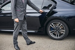 Cropped photo of a driver in a stylish suit opening the car door for his passenger