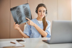 Modern doctor holding an x-ray image while having a video-call on her laptop