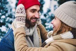 Happy bearded man and beautiful female are hugging with love while walking in park in winter