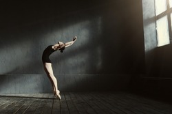 Flexible ballet dancer stretching in the dark lighted studio