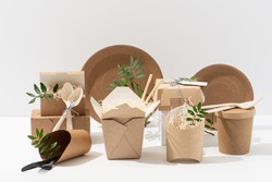 Eco friendly, disposable, recyclable, compostable tableware. Paper food boxes, dishes and flower pots with saw shawings and rowan branches in them and cornstarch cutlery over white background